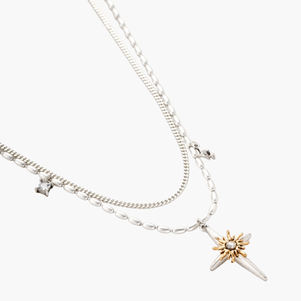 Two-layer silver-toned necklace with star charms and dagger pendant featuring golden sun motif on white background.