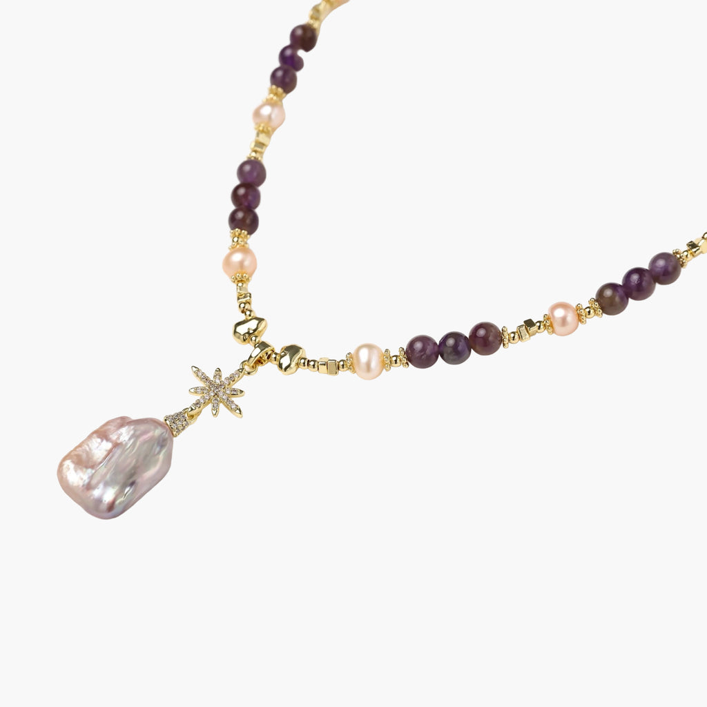 Gold necklace with iridescent baroque pearl pendant, purple amethyst beads, and crystal star charm on cream background