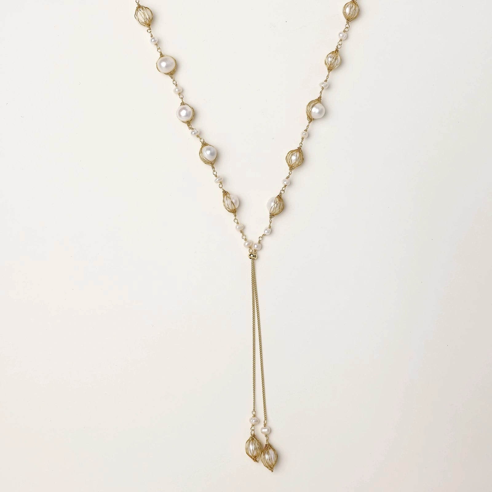 Adjustable gold lariat necklace with freshwater pearls nested in delicate cage settings and Y-shaped tassel drop
