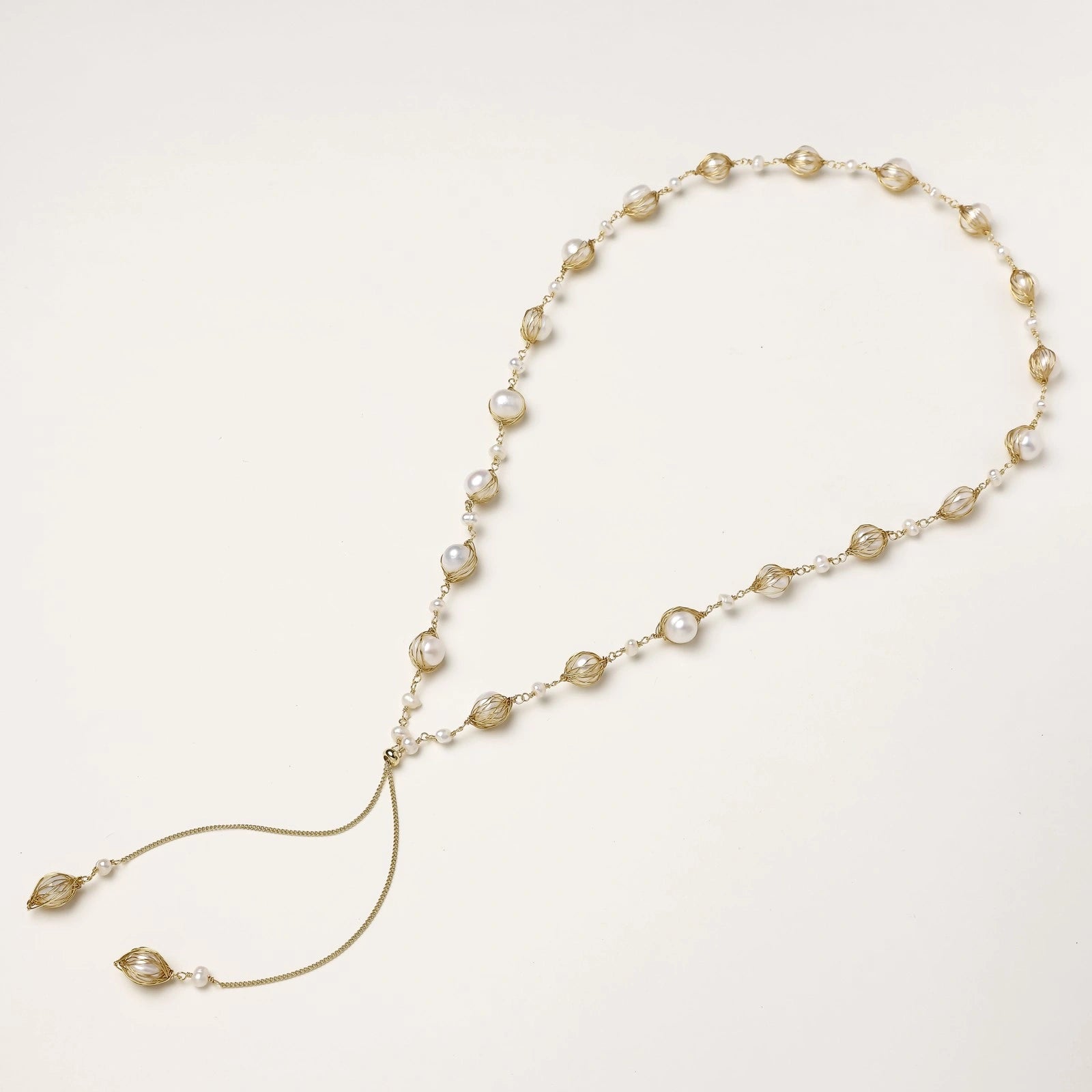 Adjustable gold lariat necklace with freshwater pearls nested in delicate cage settings and Y-shaped tassel drop