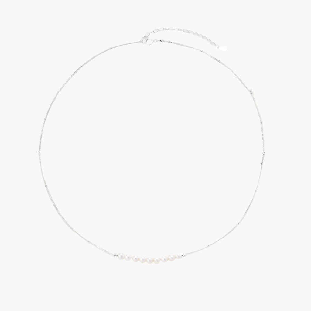 Delicate sterling silver chain necklace with small freshwater pearls arranged in a curved smile arc on cream background.