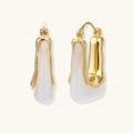 Sculptural gold-plated hoop earrings with flowing curved design and lever-back closure on cream background.
