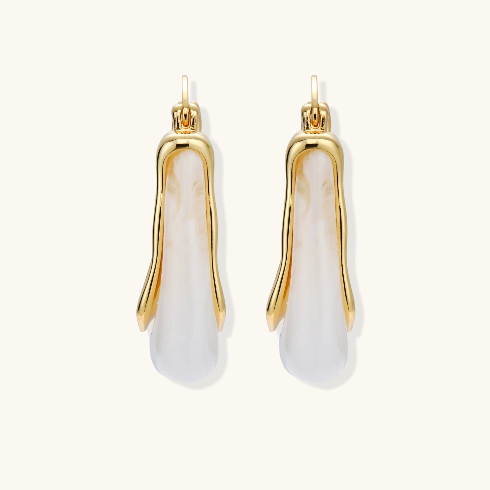 Sculptural gold-plated hoop earrings with flowing curved design and lever-back closure on cream background.