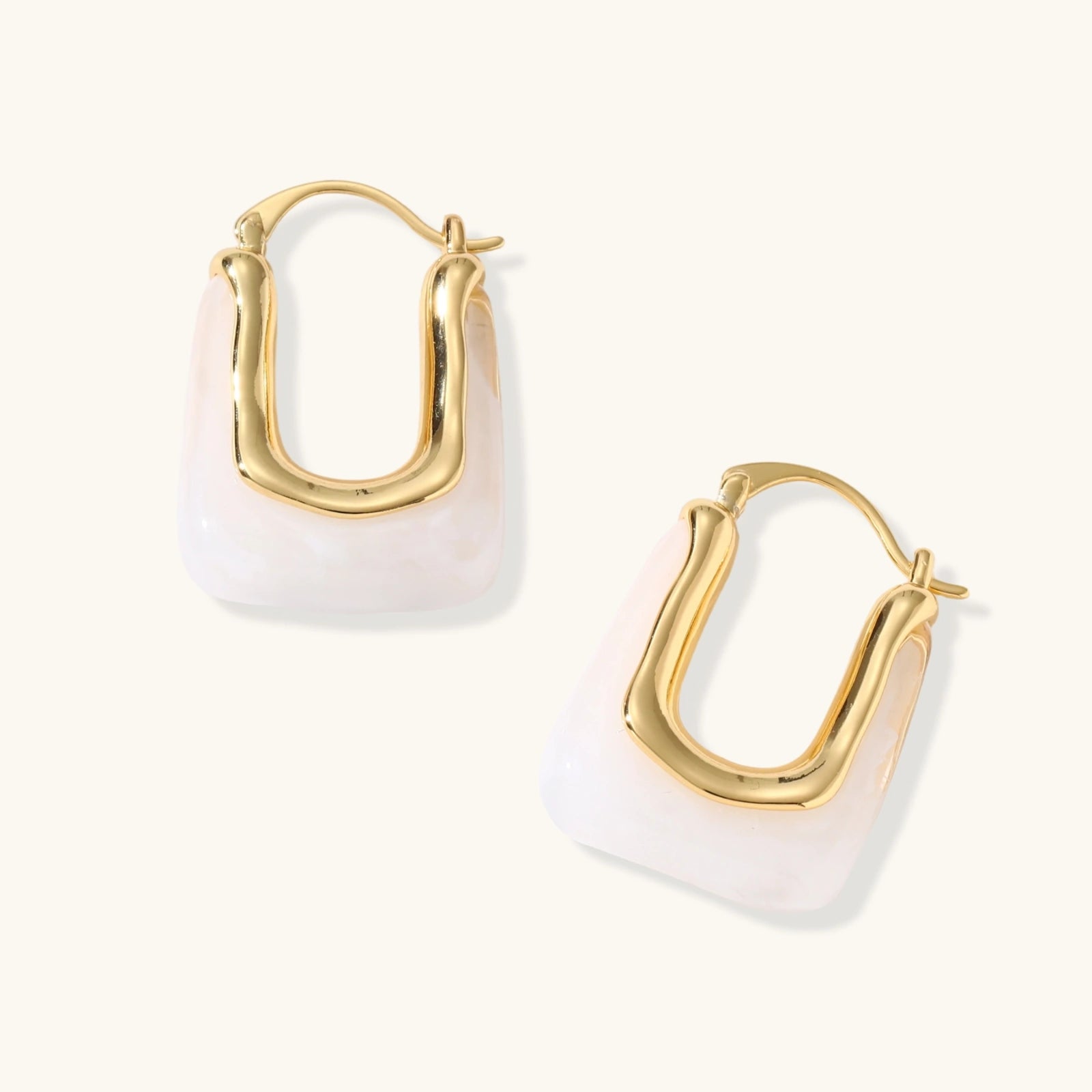 Sculptural gold-plated hoop earrings with flowing curved design and lever-back closure on cream background.