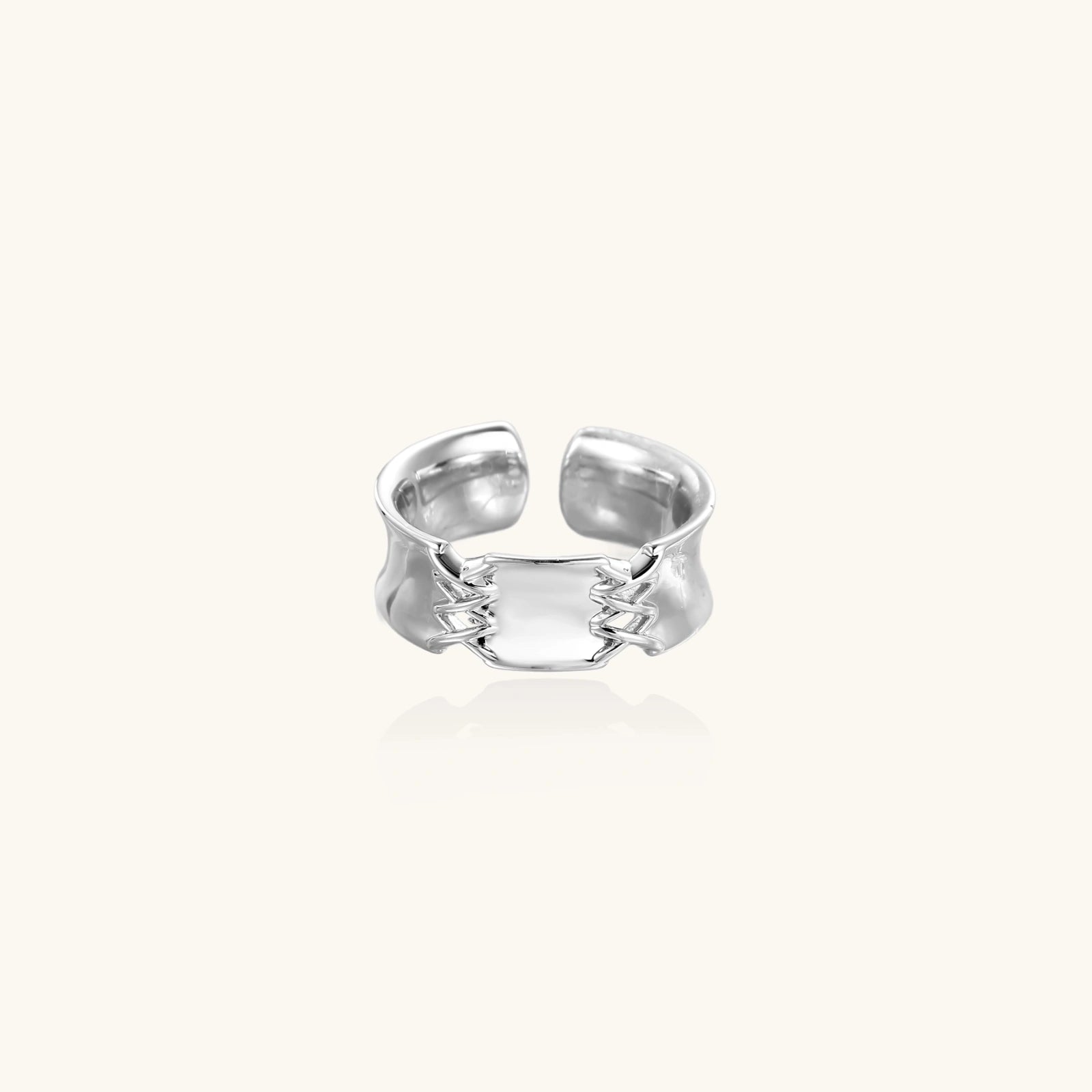 Adjustable silver-toned ring with sculptural stitch design across polished white gold-plated brass band