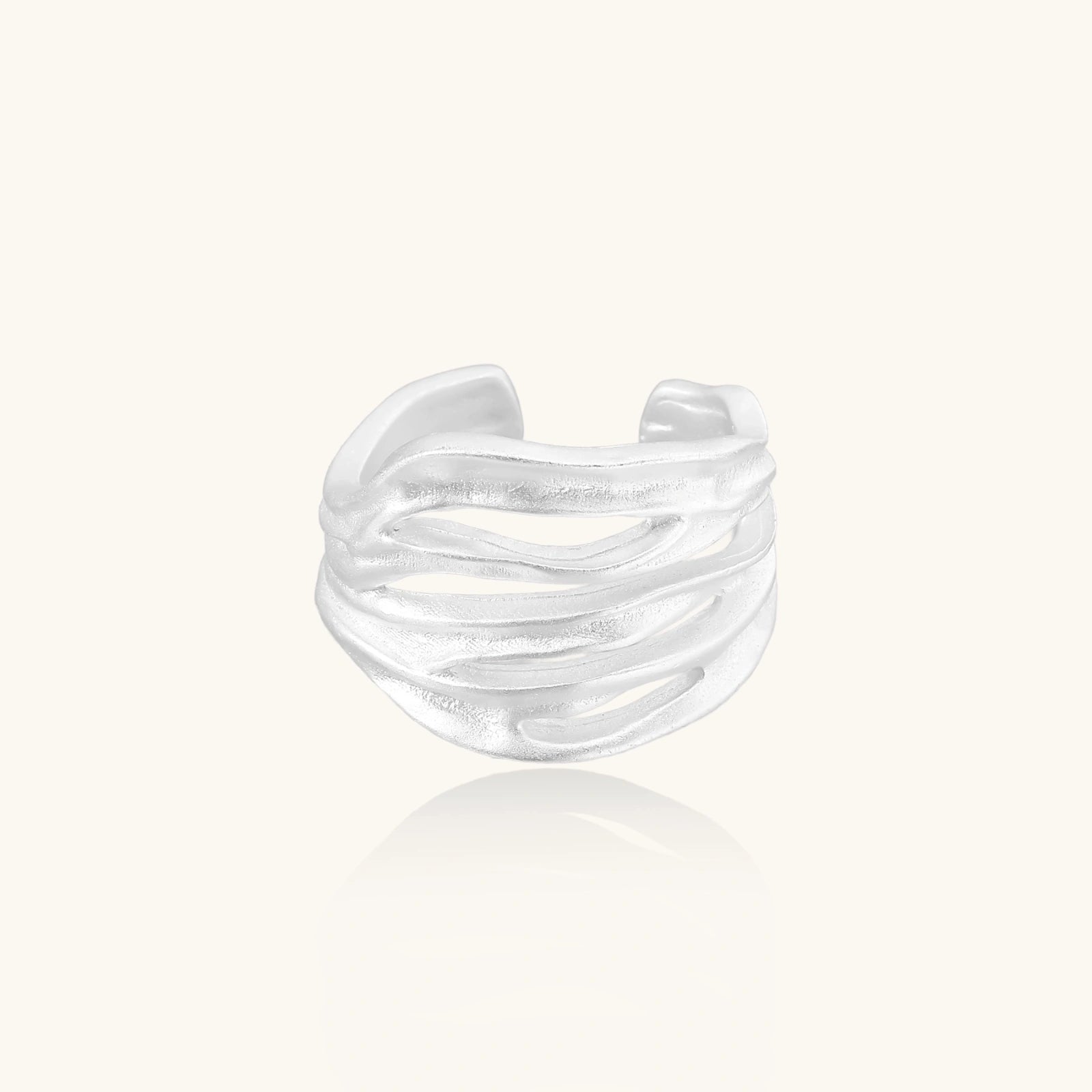 Wide sterling silver cuff ring with flowing wave patterns creating dimensional texture against cream background