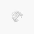Wide sterling silver cuff ring with flowing wave patterns creating dimensional texture against cream background
