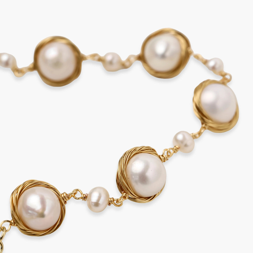 Gold wire-wrapped freshwater pearl bracelet with alternating pearl sizes on cream background, adjustable length