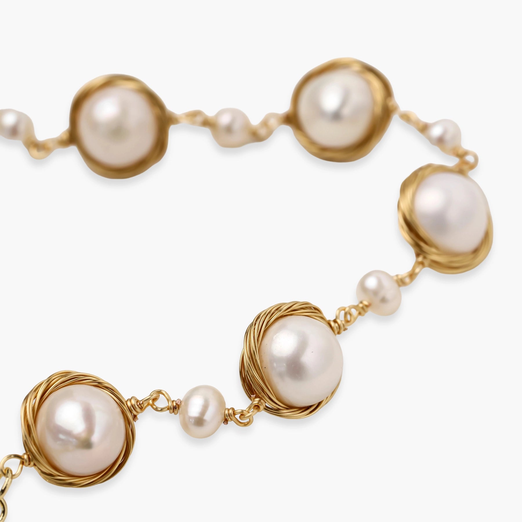 Gold wire-wrapped freshwater pearl bracelet with alternating pearl sizes on cream background, adjustable length